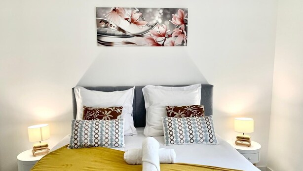 A neatly made bed with a mustard-colored throw blanket, two pillows with circular patterns, and a decorative wall piece above.