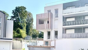A modern residential building with a flat roof, a balcony with a striped railing, and a gated driveway.