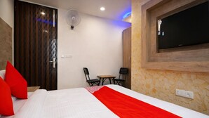 A hotel room with a bed, a TV mounted on the wall, a small table with two chairs, and a fan on the ceiling. - KDSON Vindhya Inn (New Delhi)