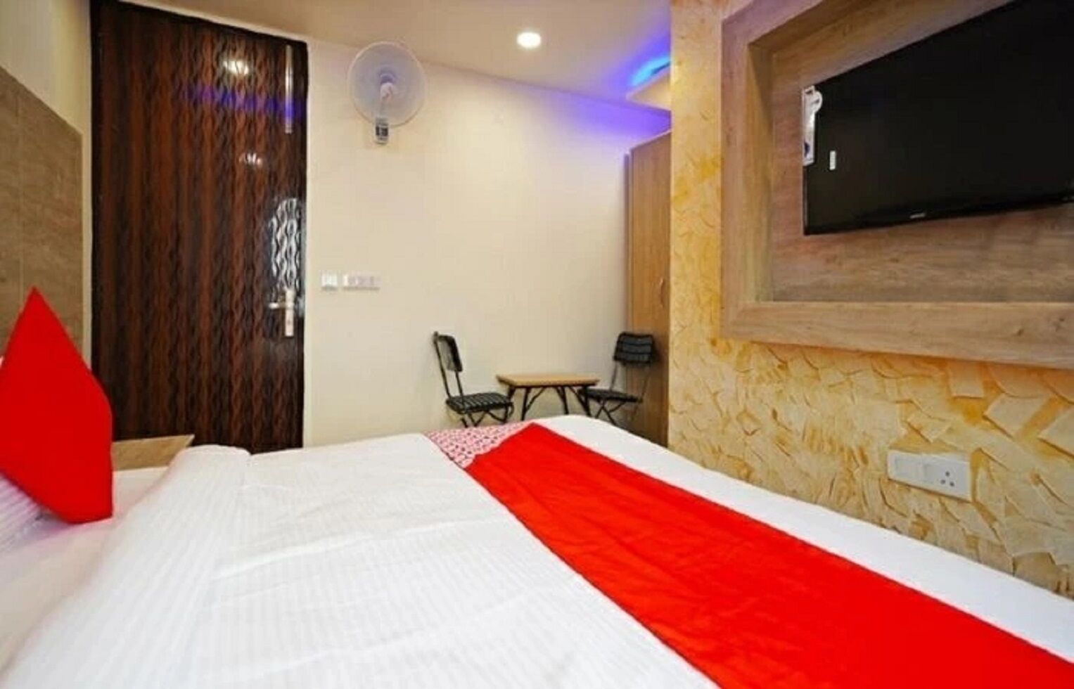 A hotel room with a bed, a TV mounted on the wall, a small table, and chairs.