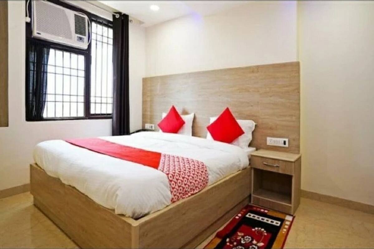 Habitación de hotel con una cama de madera, una mesita de noche, un equipo de aire acondicionado y una ventana con cortinas.
