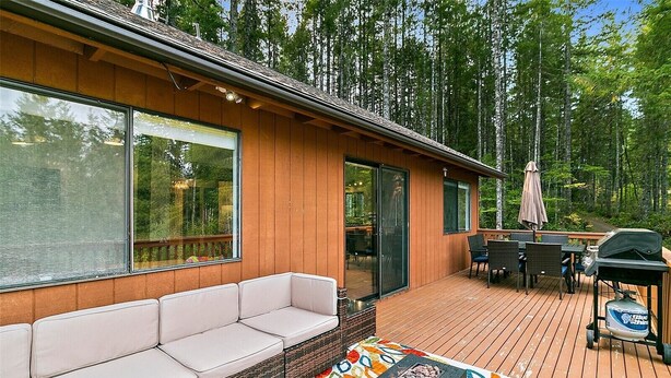 Terraza de madera con sofá y parrilla, rodeada de altos árboles.