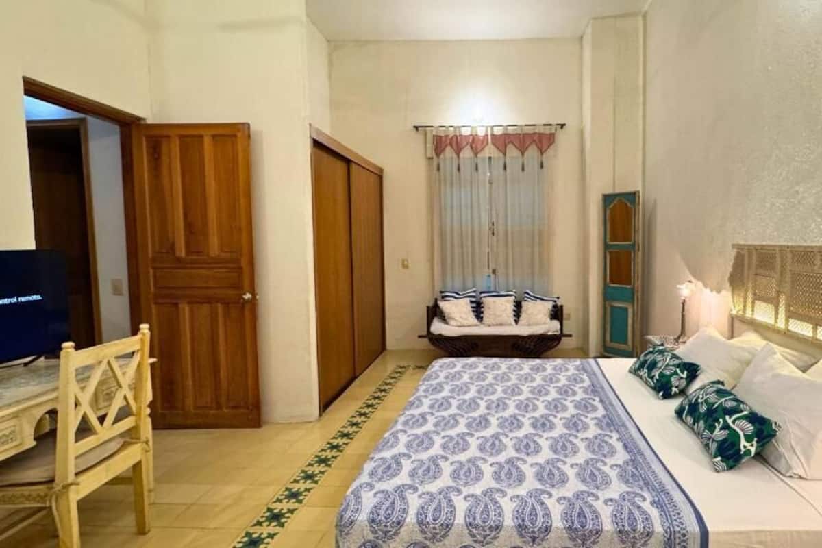Quarto com cama, cadeira de madeira, televisão e guarda-roupa.