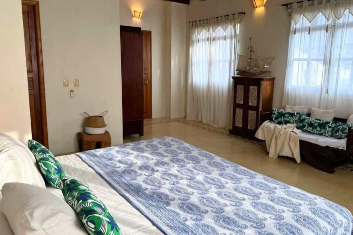 Um quarto com uma cama grande, um sofá menor, um armário de madeira e um modelo de navio sobre uma mesa.