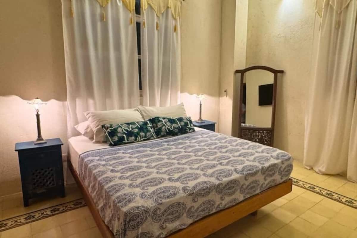 Um quarto com uma cama, duas mesas de cabeceira, um espelho e cortinas.