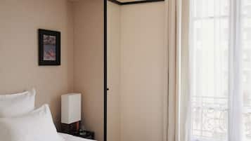 A hotel room with a bed, a nightstand, a framed picture, a window with curtains, and a view of buildings.