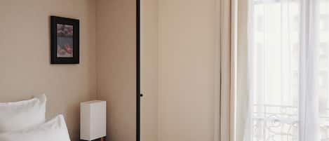 Quarto de hotel com uma cama, mesa de cabeceira, quadro emoldurado, janela com cortinas e vista para edifícios.