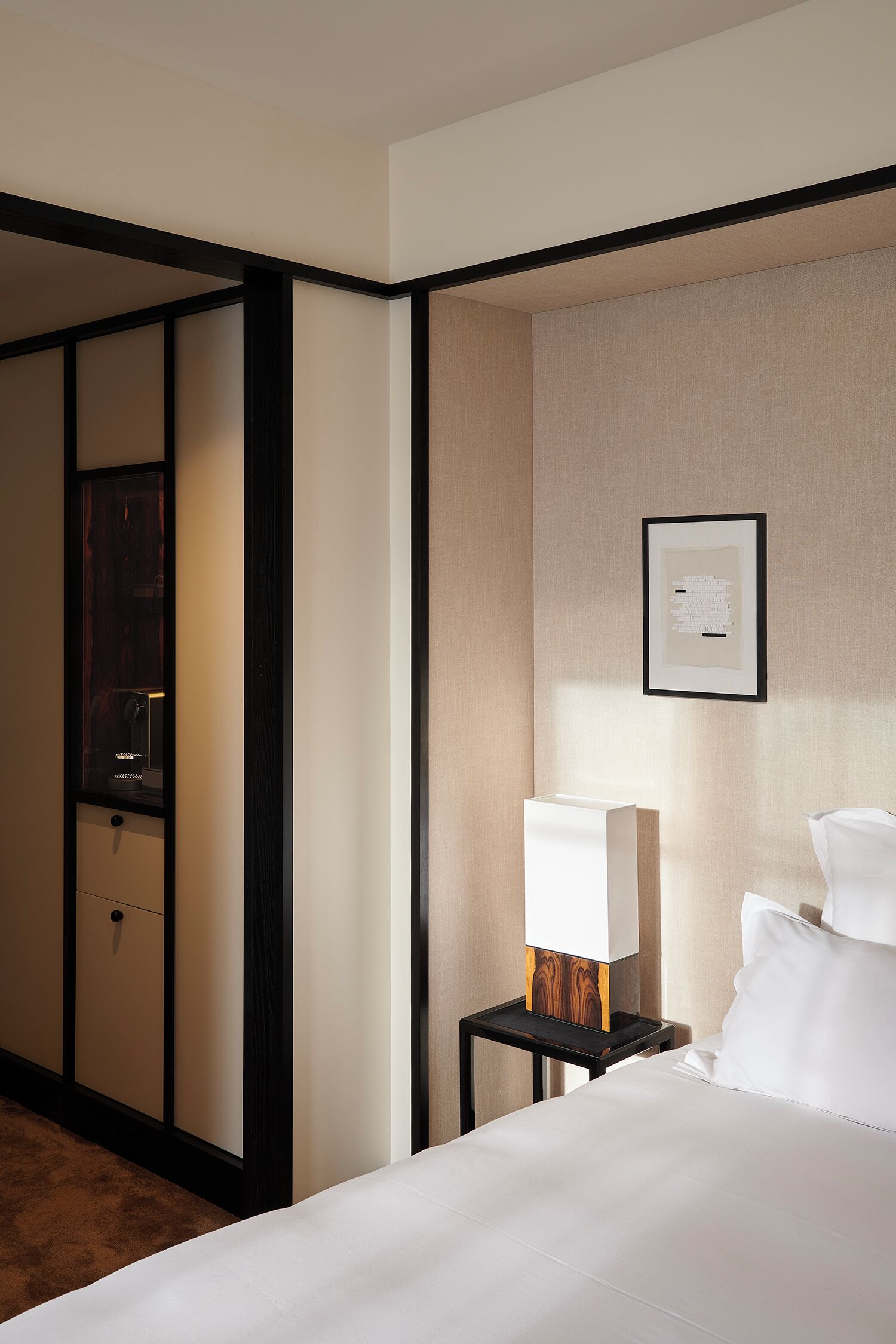 Une chambre d’hôtel avec un lit, une table de chevet avec une lampe, un tableau encadré au mur et une armoire en bois.
