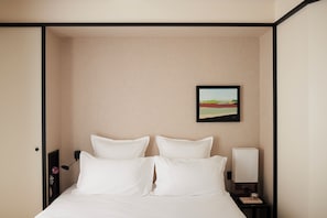 A hotel room with a bed, a nightstand with a lamp, and a framed picture on the wall. - Hôtel Atlas (Paris)