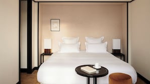 A hotel room with a large bed, two bedside tables, a round table with a book and a cup, and a brown ottoman. - Hôtel Atlas (Paris)