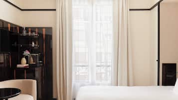 A hotel room with a bed, a desk with a computer, a chair, a wardrobe, and a window with curtains.