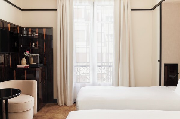 Une chambre d’hôtel comprenant un lit, un bureau avec un ordinateur, une chaise, une armoire et une fenêtre avec des rideaux.