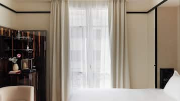 Una habitación de hotel con cama, escritorio, silla, armario y ventana con cortinas.