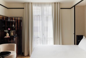 Una habitación de hotel con cama, escritorio, silla, armario y ventana con cortinas.