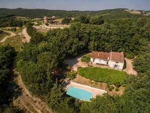 Vista aérea de una casa rodeada de vegetación densa, con una piscina y viñedos cerca.