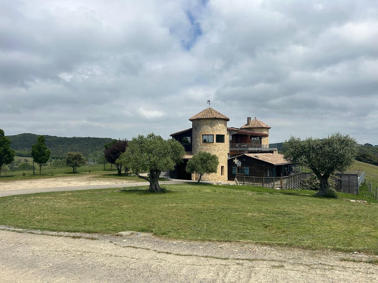 Une maison à deux étages avec une tour en pierre, entourée d’une pelouse et d’arbres.