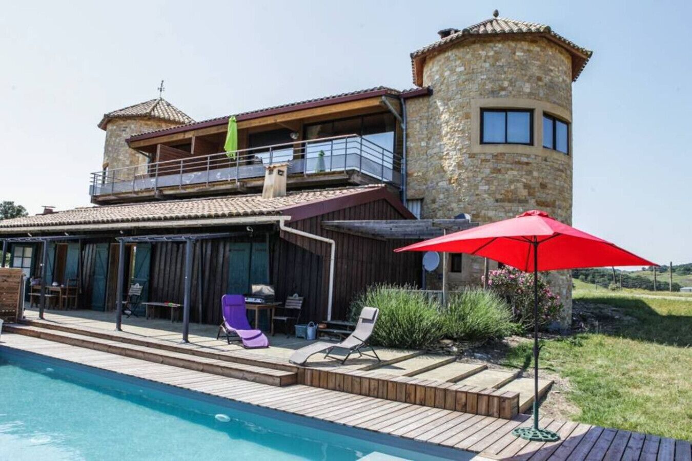 Ein zweistöckiges Steinhaus mit Pool, Sitzgelegenheiten im Freien und einem roten Sonnenschirm.