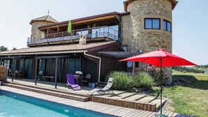 Ein zweistöckiges Steinhaus mit Pool, Sitzgelegenheiten im Freien und einem roten Sonnenschirm.
