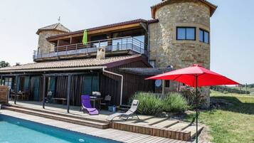 Ein zweistöckiges Steinhaus mit Pool, Sitzgelegenheiten im Freien und einem roten Sonnenschirm.