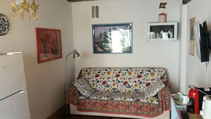 Una sala de estar con un sofá, un refrigerador, una lámpara, un cuadro enmarcado y una estantería con adornos.