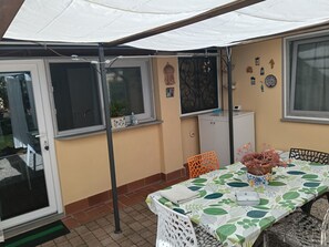 A covered patio area with a table set for dining, a chair, a potted plant, and a cabinet. - Cozy and quiet two-room apartment with garden a short distance from the sea. (Piombino)