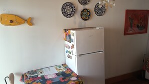 A kitchen with a refrigerator, a table with a floral tablecloth, and decorative plates on the wall. - Cozy and quiet two-room apartment with garden a short distance from the sea. (Piombino)