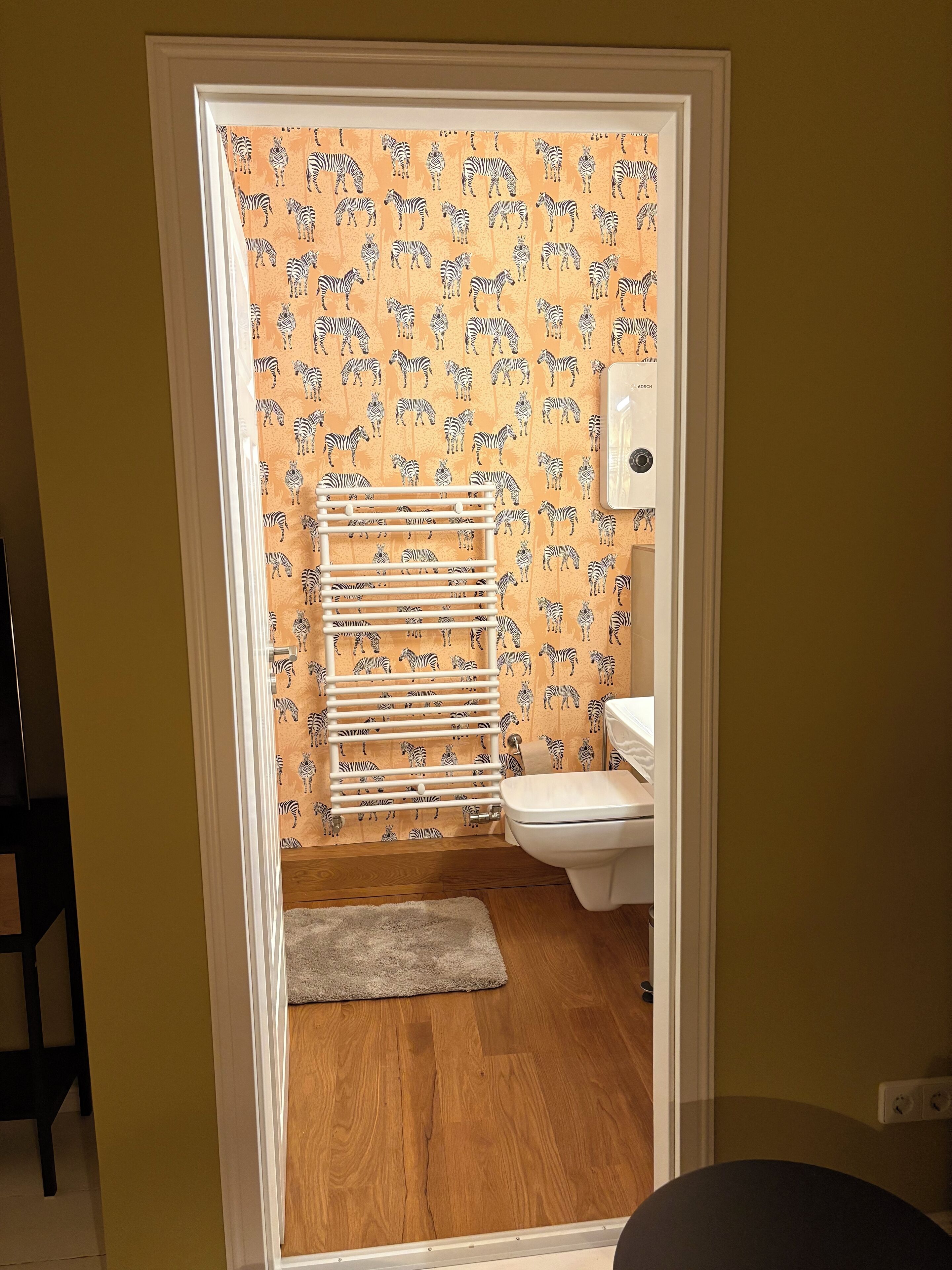 Ein Badezimmer mit zebraartig gemustertem Wandpapier, einem weißen Heizkörper und einer weißen Toilette.