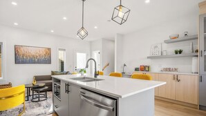 A modern kitchen with a central island, stainless steel appliances, and a bright, minimalist design. - New 1500 ft² Home w/ AC & Garage | 7 mins to DT (Calgary)