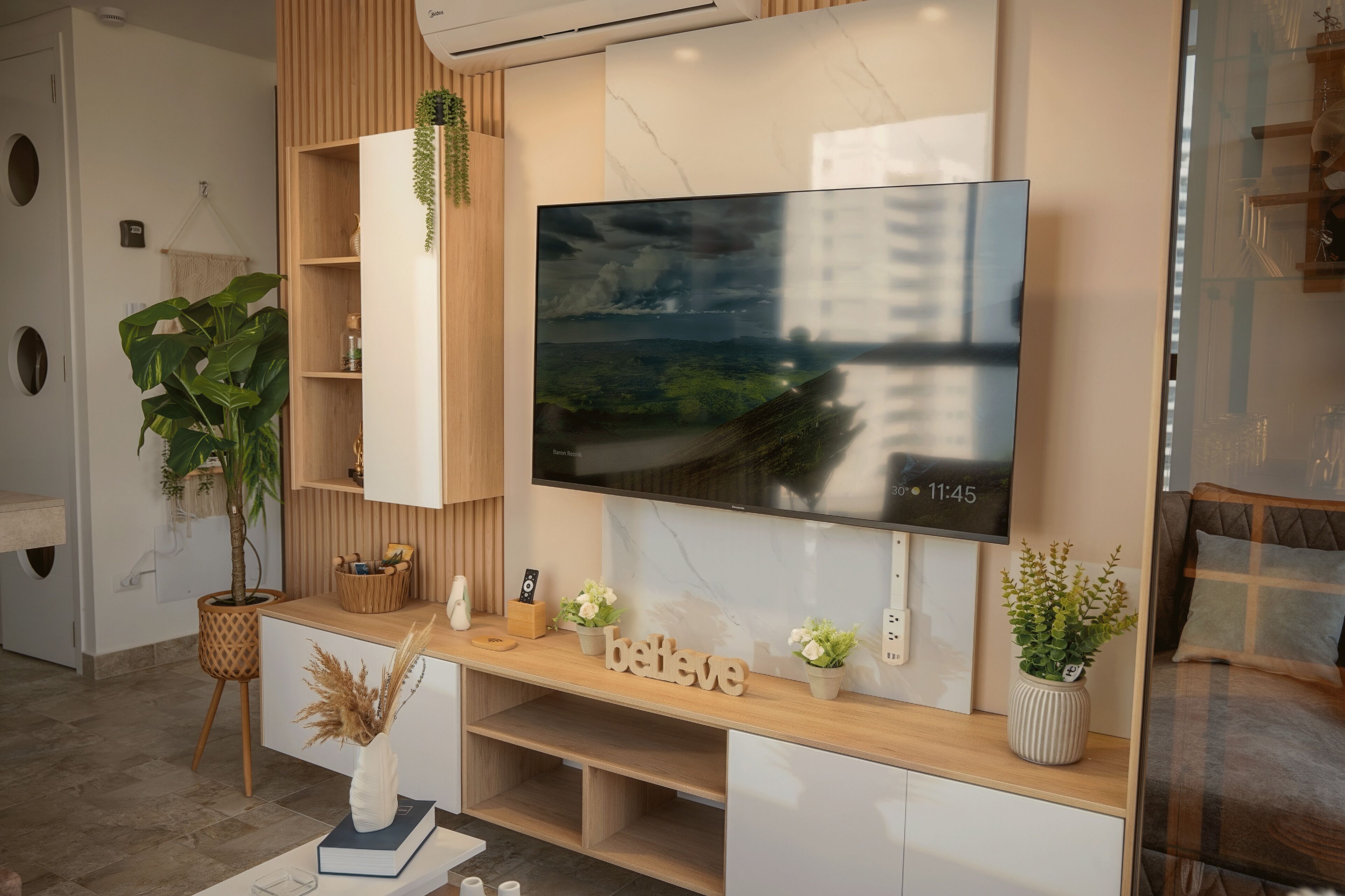 A modern living room with a large flat-screen TV mounted on a wooden wall, a wooden console table with decorative items, and a comfortable seating area with a sofa and a coffee table.