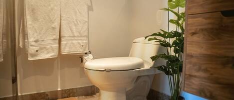 A modern bathroom with a white toilet, a towel rack with two towels, a potted plant, and a wooden cabinet.