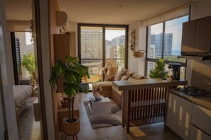 Eine moderne Wohnung mit Küche, Essbereich und Wohnzimmer. Sie verfügt über große Fenster, ein Sofa, einen Couchtisch und einen Topfpflanze.