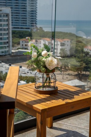 Ein Holztisch mit einer Glasvase, die weiße Blumen enthält, vor einer Stadtkulisse.