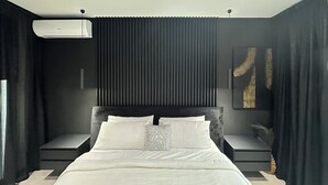 Ein modernes Schlafzimmer mit einem großen Bett, dunklen Vorhängen, einem Deckenventilator und einer Wand-Klimaanlage.