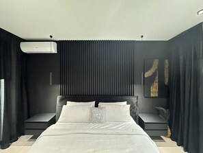 Ein modernes Schlafzimmer mit einem großen Bett, dunklen Vorhängen, einem Deckenventilator und einer Wand-Klimaanlage.