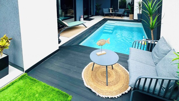 Ein moderner Poolbereich im Freien mit minimalistischem Design, inklusive Pool, Liegestühlen und einem kleinen Tisch.