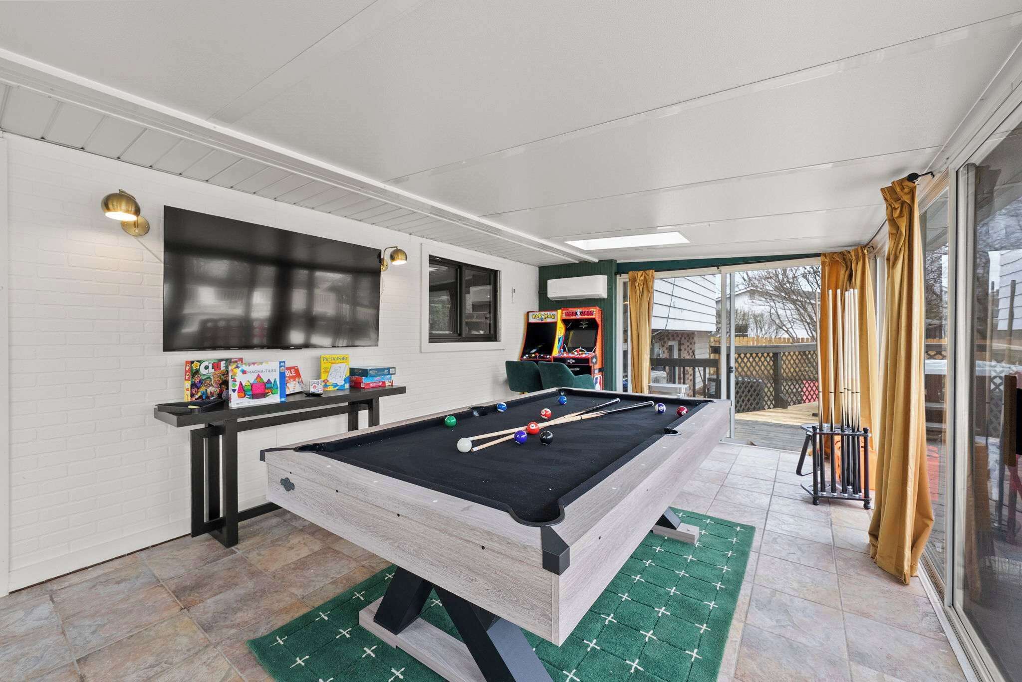 A pool table with billiard balls and cues, a green mat, and a television on the wall.