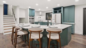A modern kitchen with a central island, bar stools, and a staircase leading to an upper level. - Pickleball-Basketball-Pool-HotTub-GameRoom-FirePit (Columbus)