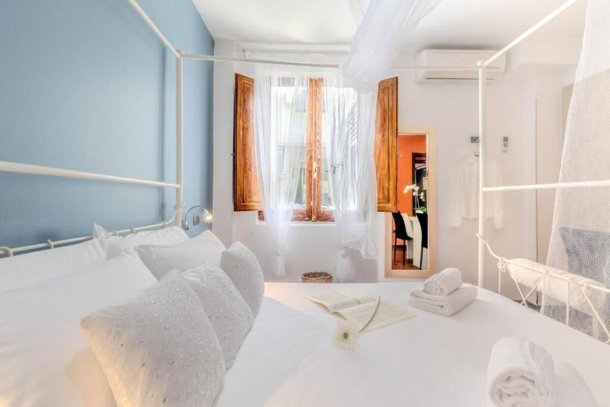 Une chambre d’hôtel avec un lit, une fenêtre avec des rideaux, un miroir et une petite table avec des serviettes.