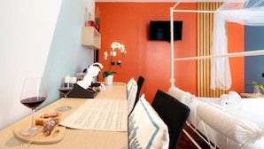 Hotelkamer met een bed, een bureau met een computer, een stoel, een tafel met wijnglazen en een menukaart, en een televisie aan de muur.
