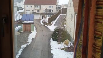 Blick aus dem Fenster auf eine Wohnstraße mit Häusern, einer asphaltierten Straße und Solaranlage auf einem Dach.