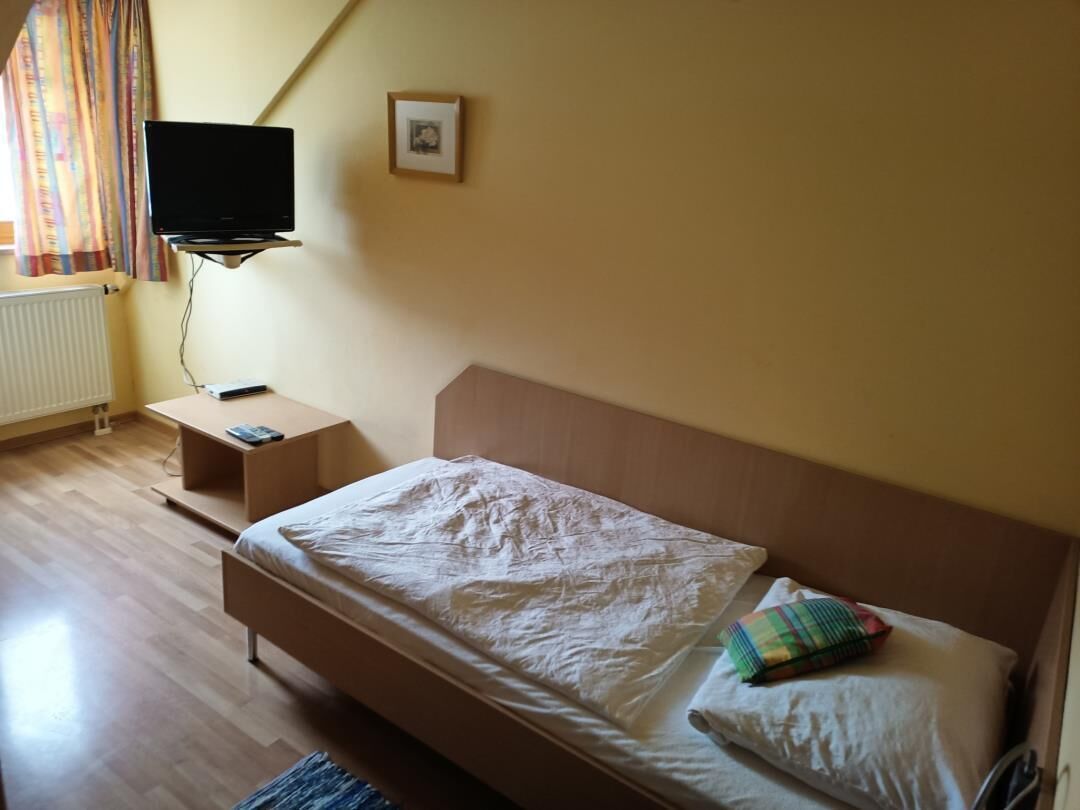 Ein Schlafzimmer mit Bett, Wand-Fernseher, Nachttisch und einem Fenster mit Vorhängen.