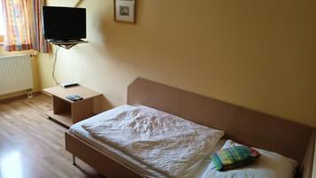Ein Schlafzimmer mit Bett, Wand-Fernseher, Nachttisch und einem Fenster mit Vorhängen.
