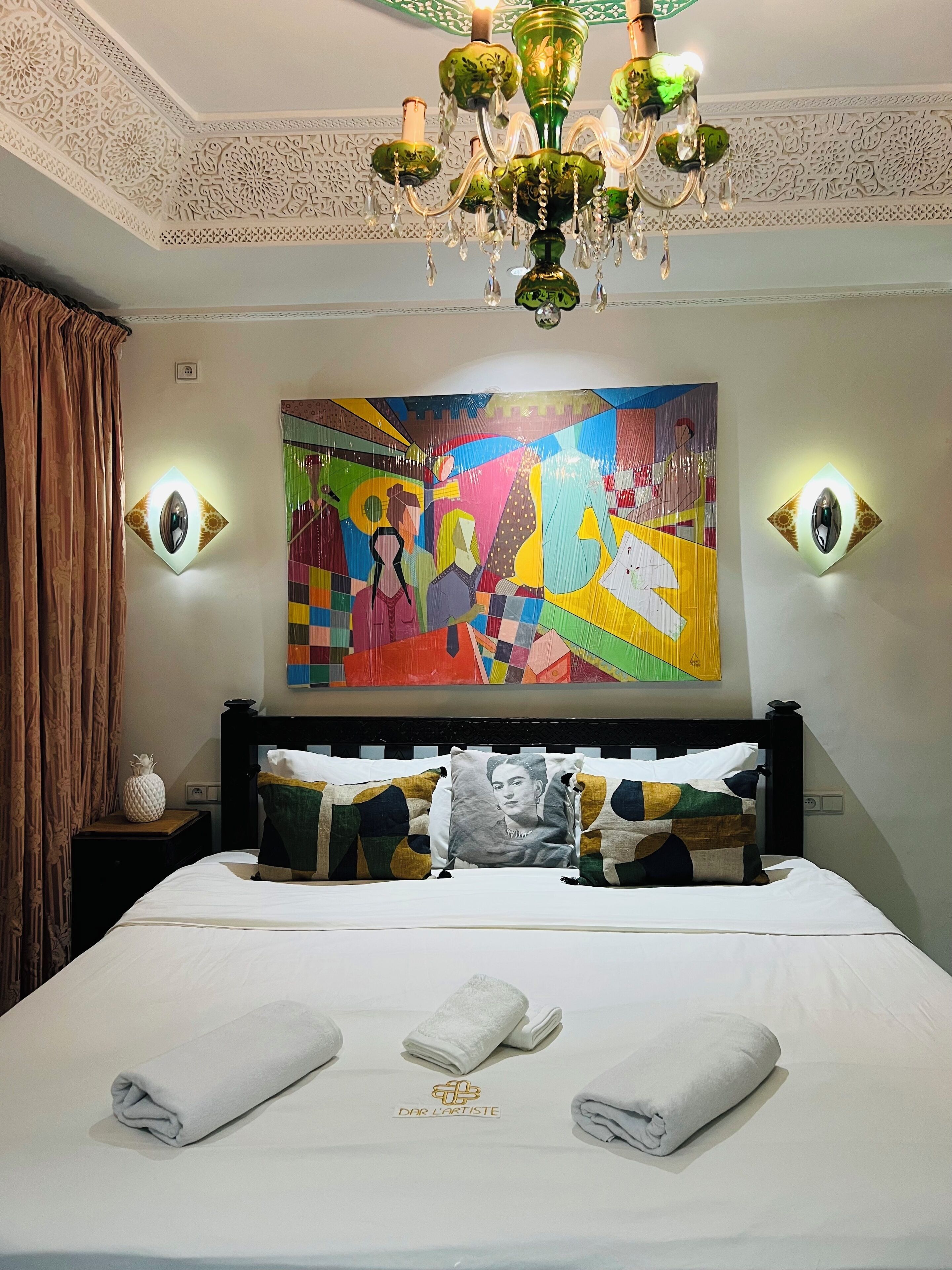 Ein Hotelzimmer mit einem Bett, einer Kristalllüster, einem farbenfrohen abstrakten Gemälde und zwei Wandleuchten.