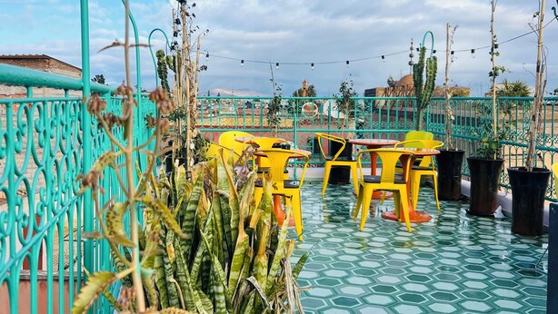 Terraza en la azotea con suelo de patrón hexagonal, sillas amarillas y anaranjadas, y plantas en macetas.