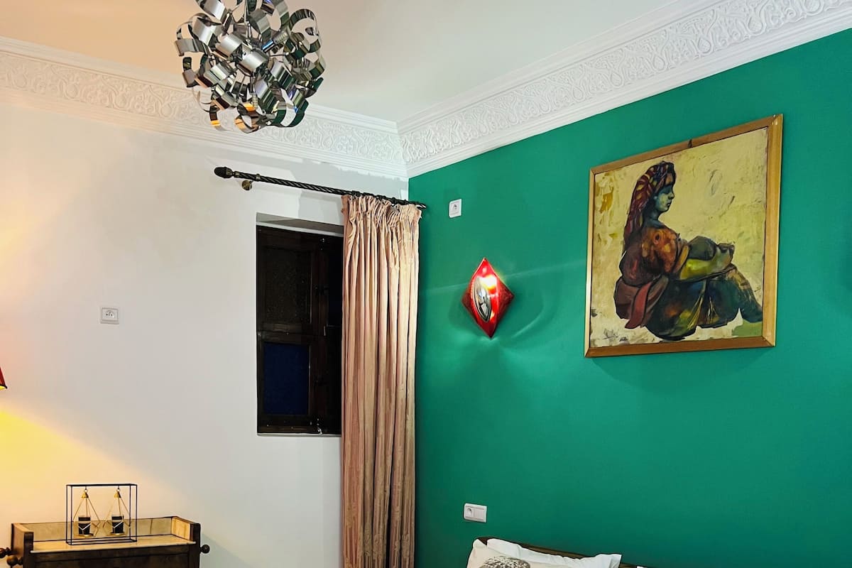 Cama bem arrumada com lençóis brancos, cabeceira de madeira e parede verde com um quadro emoldurado.