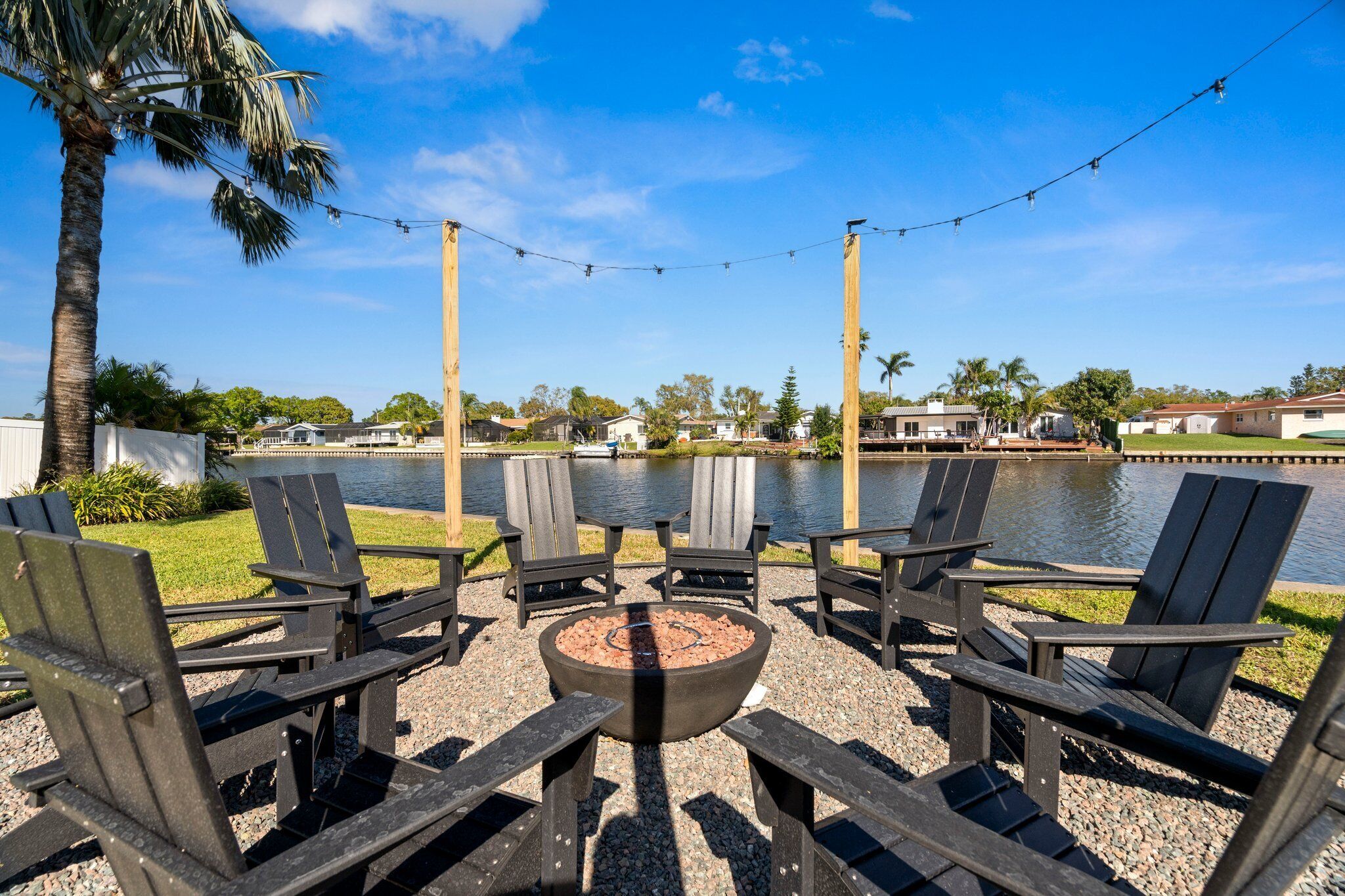 Un patio junto al lago con sillas Adirondack y un brasero, con vistas despejadas al lago y edificios residenciales.
