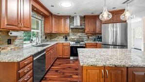 Cozinha com armários de madeira, bancadas de granito, eletrodomésticos de aço inoxidável e backsplash de tijolos.