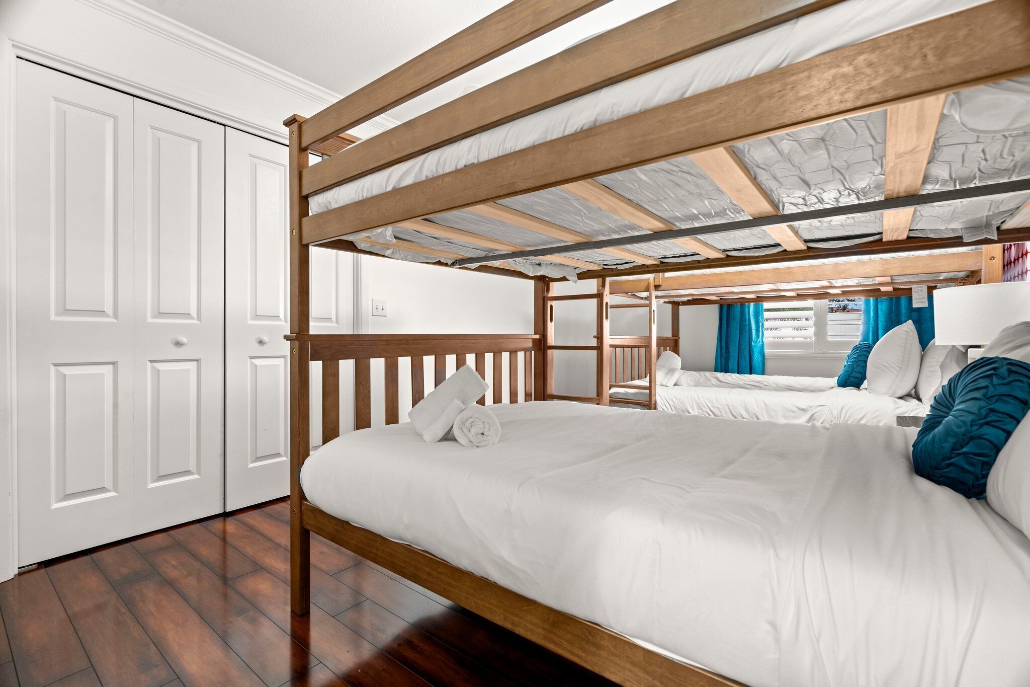 A bunk bed room with white walls, wooden ceiling beams, and a wooden floor.
