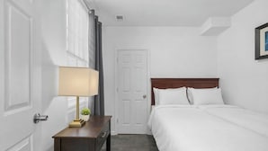 A hotel room with a bed, a bedside table with a lamp, a door, and a framed picture on the wall. - Charming 3-bedroom Home in Southwest Detroit (Detroit)