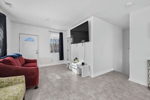 A modern living room with a red sofa, a green patterned sofa, a white entertainment unit, and a flat-screen TV. - Charming 3-bedroom Home in Southwest Detroit (Detroit)